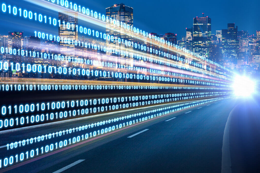 A blurred cityscape at night with streaks of light representing data in binary code. The scene captures the intersection of technology and urban life, emphasizing speed and connectivity.