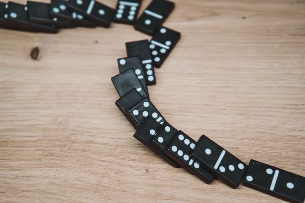 Black dominoes with white dots arranged in a curved line on a wooden surface.